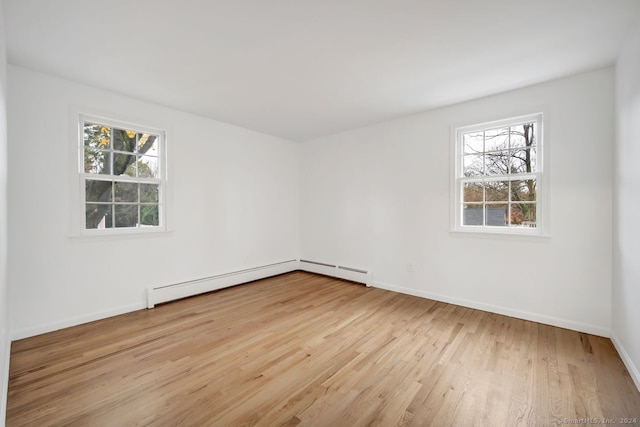 empty room featuring baseboard heating, light hardwood / wood-style flooring, and a healthy amount of sunlight