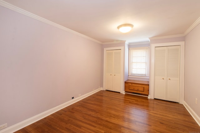 unfurnished bedroom with dark hardwood / wood-style floors, multiple closets, and crown molding