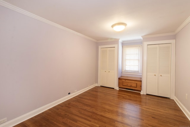 unfurnished bedroom with dark wood-type flooring, ornamental molding, baseboards, and two closets