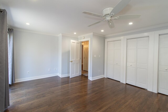 unfurnished bedroom with ceiling fan, dark hardwood / wood-style flooring, ornamental molding, and two closets