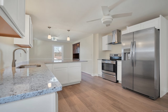 kitchen with stainless steel appliances, wall chimney range hood, light hardwood / wood-style flooring, white cabinets, and hanging light fixtures