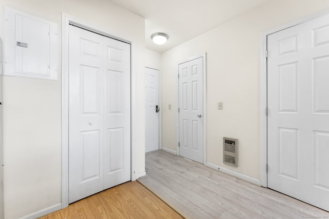 hall featuring electric panel, light hardwood / wood-style floors, and heating unit