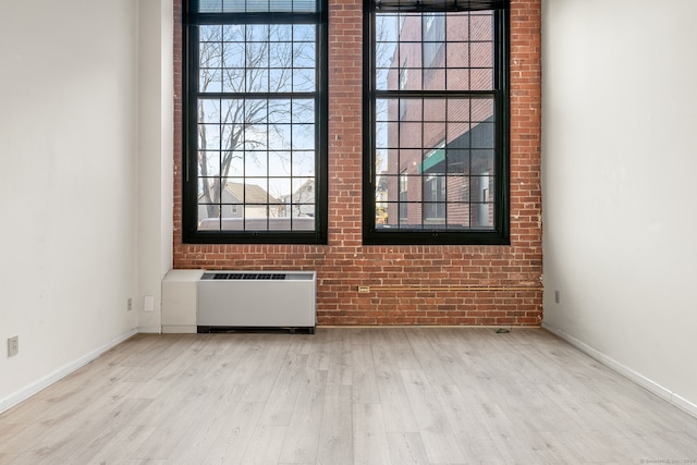 unfurnished room with radiator heating unit, brick wall, and light wood-type flooring