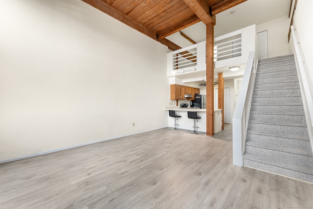 unfurnished living room featuring a high ceiling, light hardwood / wood-style floors, wooden ceiling, and beam ceiling