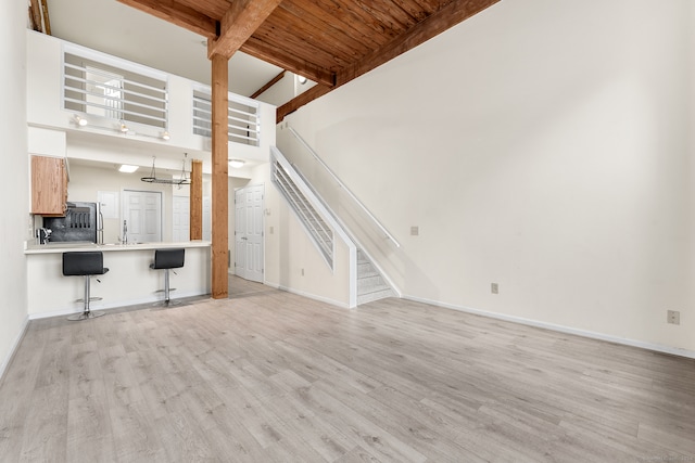 unfurnished living room with beam ceiling, a towering ceiling, wood ceiling, and light hardwood / wood-style floors