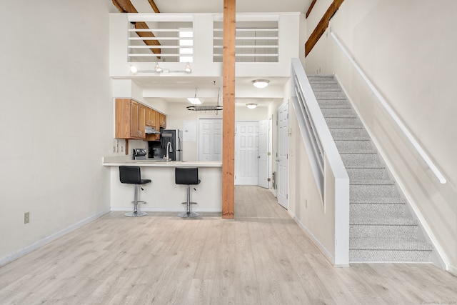 kitchen with black refrigerator, a high ceiling, a breakfast bar, and light hardwood / wood-style floors