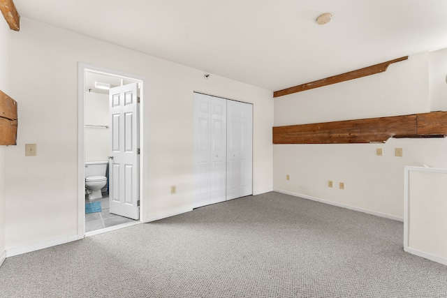 unfurnished bedroom with beam ceiling, light carpet, a closet, and ensuite bathroom