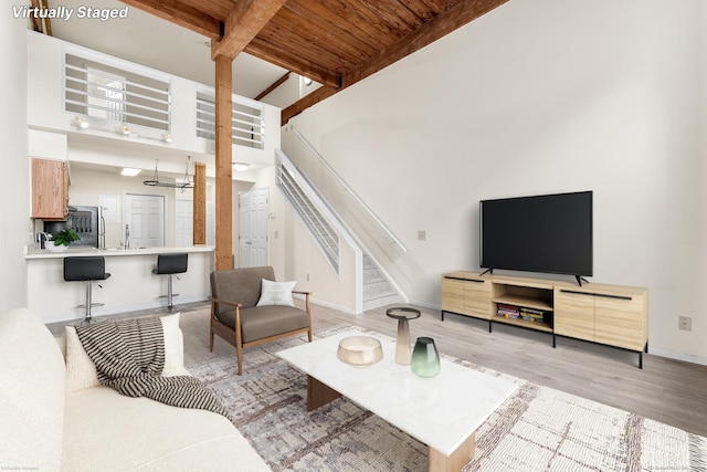 living room featuring beam ceiling, wooden ceiling, a high ceiling, and light hardwood / wood-style floors