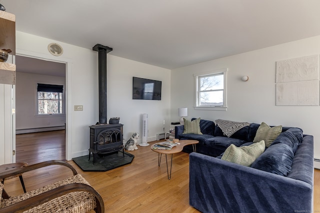 living room with light wood-type flooring, a wood stove, a wealth of natural light, and a baseboard heating unit