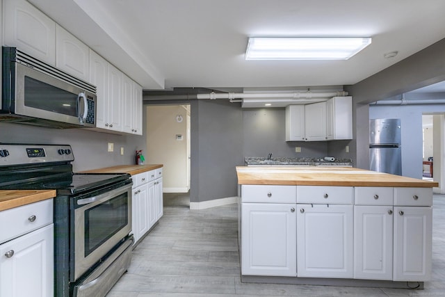 kitchen with baseboards, light wood-style flooring, appliances with stainless steel finishes, wood counters, and white cabinetry