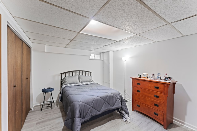 bedroom with a drop ceiling, light hardwood / wood-style flooring, and a closet