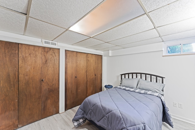 bedroom featuring multiple closets, a paneled ceiling, and light wood-type flooring