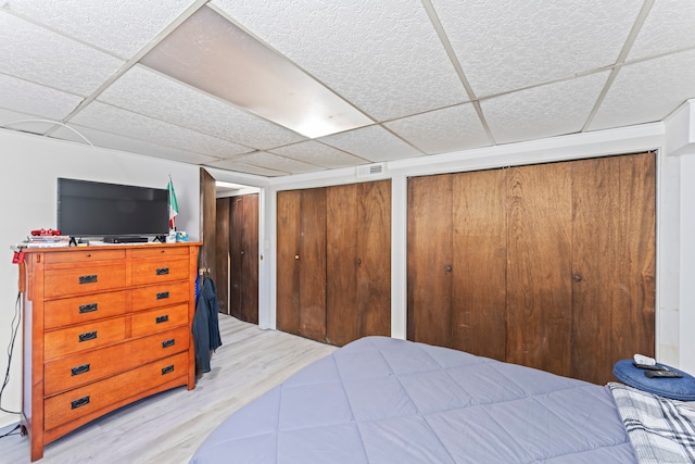 bedroom featuring a drop ceiling, light wood-type flooring, and multiple closets