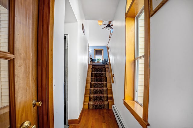 stairs with wood-type flooring and a baseboard heating unit