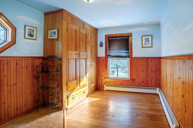 interior space featuring light wood-type flooring, baseboard heating, and wooden walls