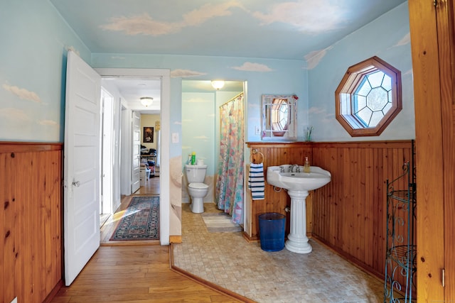 bathroom with hardwood / wood-style flooring, a shower with shower curtain, toilet, and wooden walls