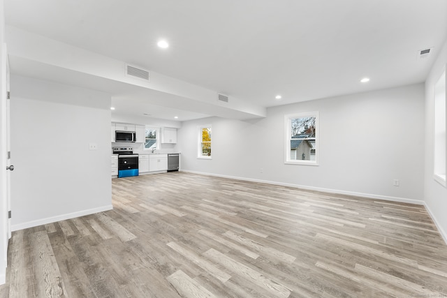 unfurnished living room featuring plenty of natural light, light hardwood / wood-style floors, and sink