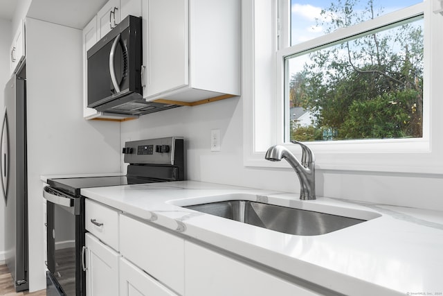 kitchen featuring white cabinetry, sink, stainless steel appliances, light stone counters, and light hardwood / wood-style floors