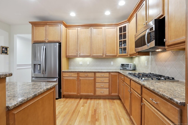 kitchen with light stone counters, light wood-type flooring, appliances with stainless steel finishes, and tasteful backsplash