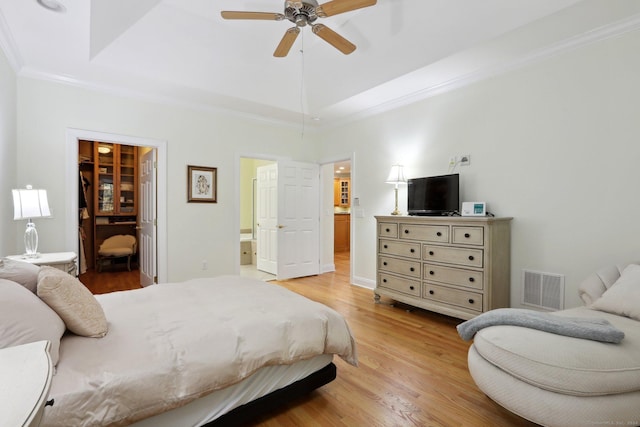 bedroom featuring a walk in closet, ensuite bath, ornamental molding, ceiling fan, and light hardwood / wood-style flooring