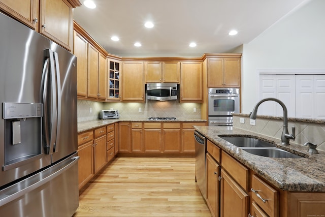 kitchen with tasteful backsplash, stainless steel appliances, sink, stone countertops, and light hardwood / wood-style floors