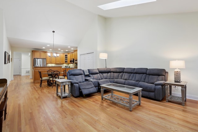 living room featuring a notable chandelier, light wood-type flooring, high vaulted ceiling, and a skylight