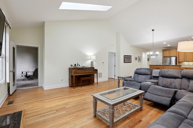 living room with high vaulted ceiling, a skylight, light hardwood / wood-style flooring, and a notable chandelier