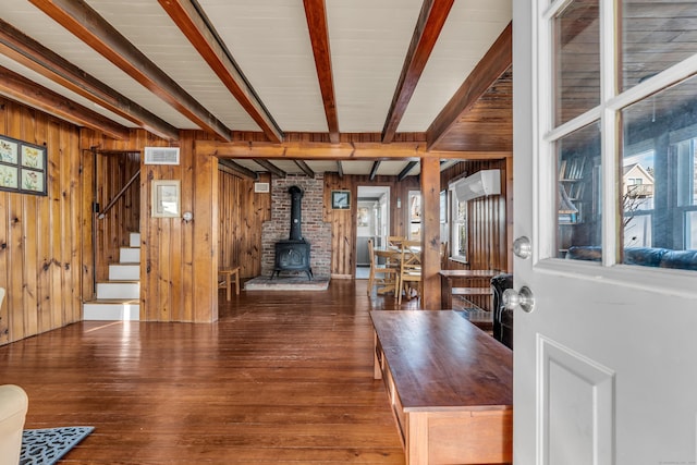 foyer entrance featuring a wood stove, wood walls, beamed ceiling, and dark wood-type flooring