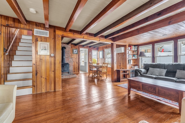 living room with beamed ceiling, hardwood / wood-style flooring, a wood stove, and wooden walls