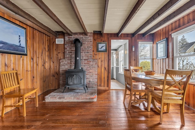 dining room featuring hardwood / wood-style flooring, beam ceiling, wood walls, and a wood stove