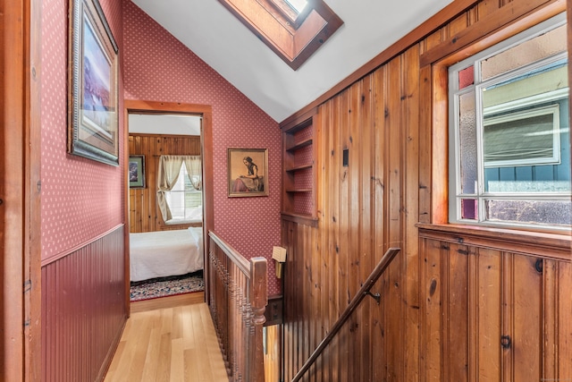 corridor with light hardwood / wood-style floors, built in features, and lofted ceiling with skylight