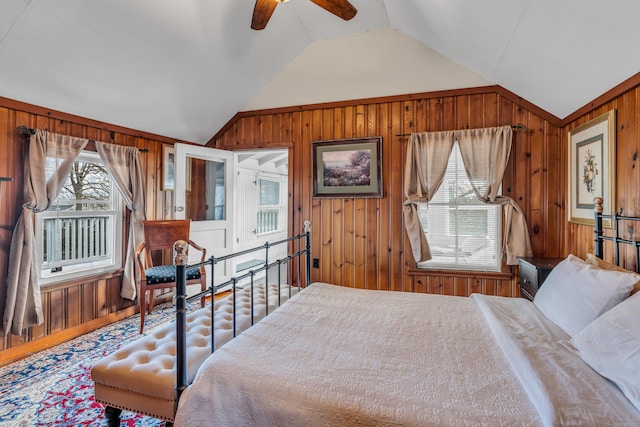 bedroom with vaulted ceiling, multiple windows, wood walls, and ceiling fan