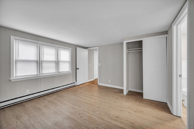 unfurnished bedroom with light hardwood / wood-style floors, baseboard heating, connected bathroom, and a closet