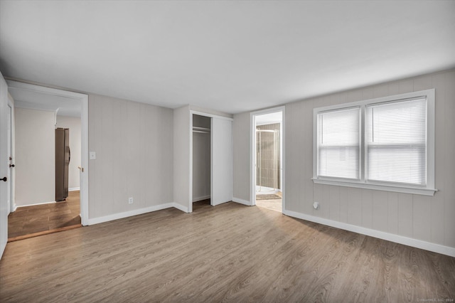 unfurnished bedroom with ensuite bathroom, light hardwood / wood-style floors, stainless steel refrigerator, and a closet