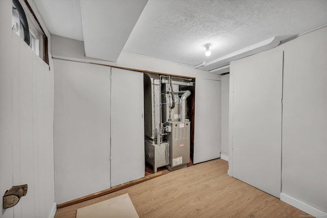 basement with heating unit, light hardwood / wood-style floors, and a textured ceiling