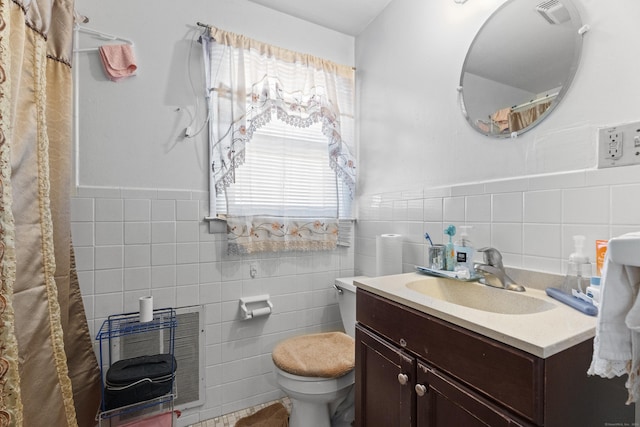 bathroom featuring heating unit, vanity, tile walls, and toilet