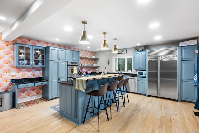 kitchen featuring light hardwood / wood-style flooring, blue cabinetry, decorative light fixtures, a kitchen bar, and stainless steel appliances