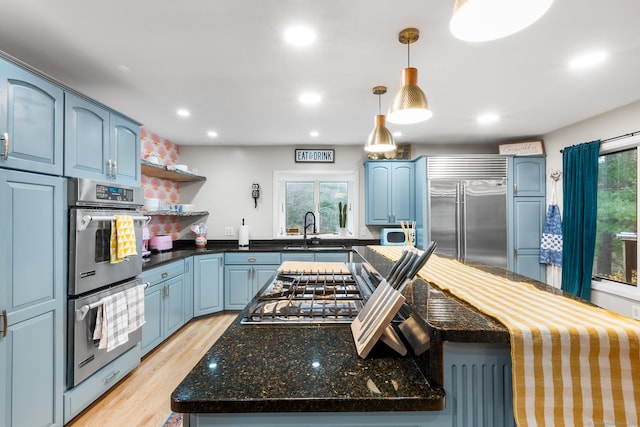 kitchen with blue cabinetry, hanging light fixtures, stainless steel appliances, and sink