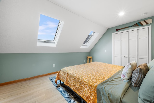 bedroom with light wood-type flooring, a closet, and vaulted ceiling with skylight