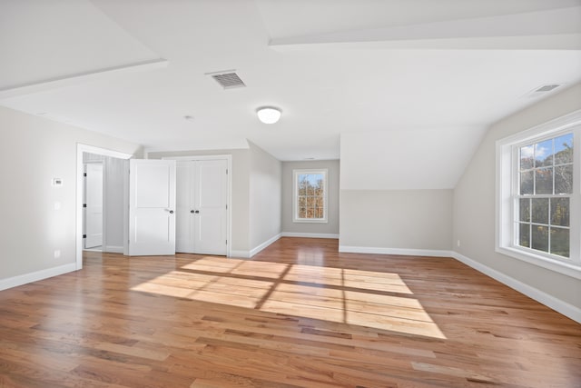 additional living space with a healthy amount of sunlight, vaulted ceiling, and light hardwood / wood-style flooring