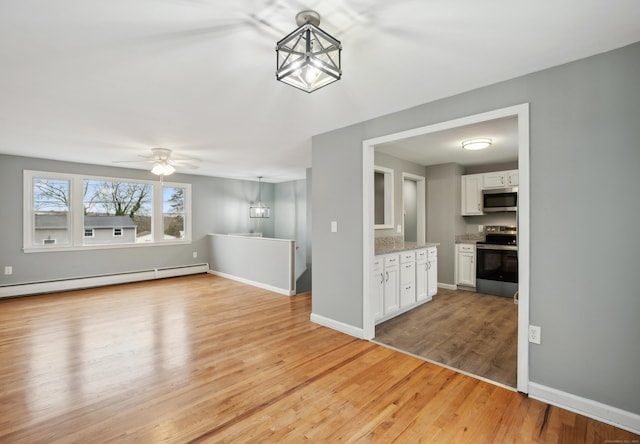 unfurnished living room featuring ceiling fan with notable chandelier, light wood-type flooring, and baseboard heating