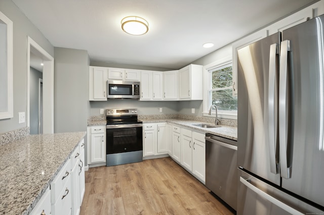 kitchen with sink, light wood-type flooring, light stone counters, white cabinetry, and stainless steel appliances