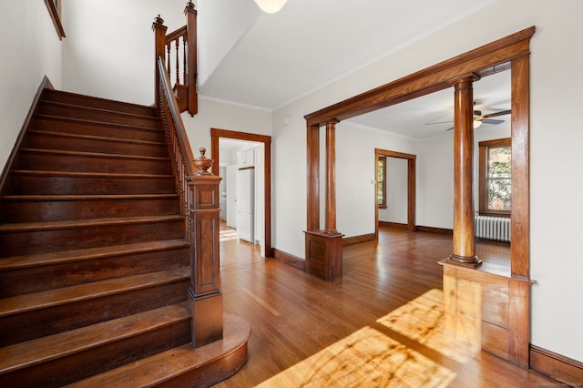 stairway featuring ornate columns, ceiling fan, radiator heating unit, wood-type flooring, and ornamental molding