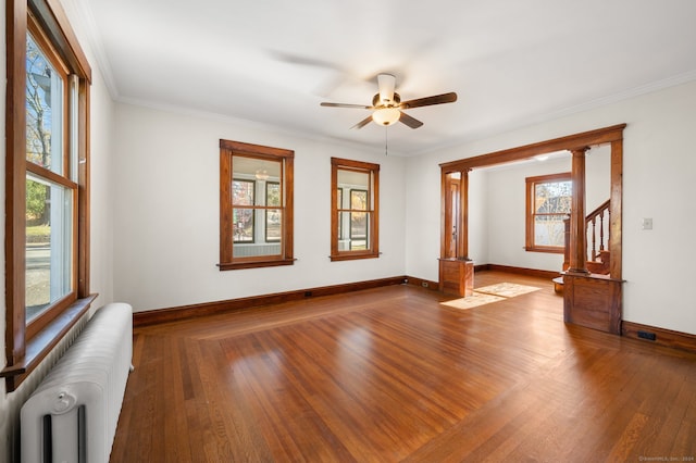 empty room with hardwood / wood-style floors, plenty of natural light, radiator heating unit, and ornamental molding