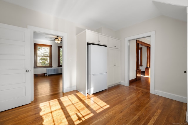 unfurnished bedroom featuring wood-type flooring, white fridge, radiator, and lofted ceiling