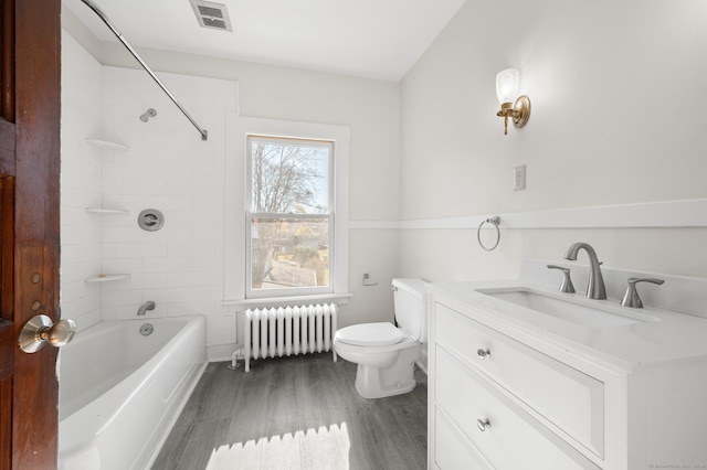 full bathroom featuring vanity, radiator, tiled shower / bath combo, toilet, and wood-type flooring