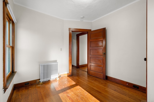 empty room with crown molding, radiator heating unit, a textured ceiling, and hardwood / wood-style flooring