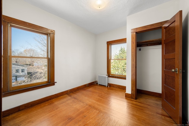 unfurnished bedroom featuring a closet, radiator heating unit, wood-type flooring, and a textured ceiling