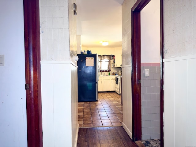 corridor with tile walls, dark wood-type flooring, and sink