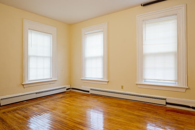 unfurnished room featuring hardwood / wood-style floors, baseboard heating, and a wealth of natural light